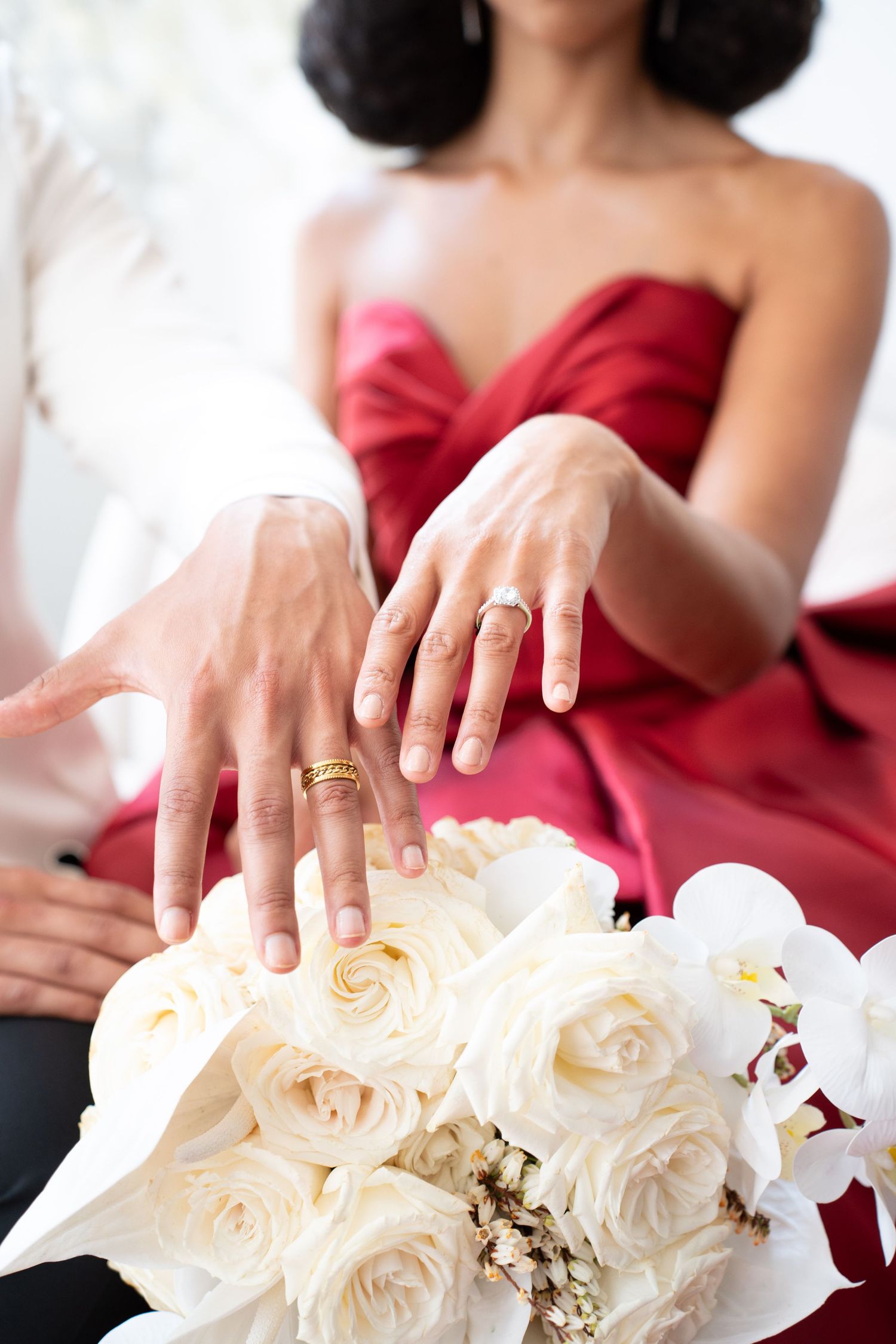 Newlyweds showing gold wedding bands above elegant white rose and orchid bridal bouquet.