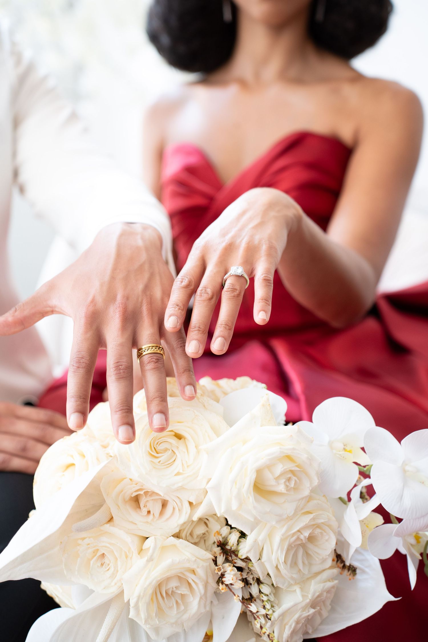 Bride and groom displaying gold wedding rings above white rose and orchid bouquet.