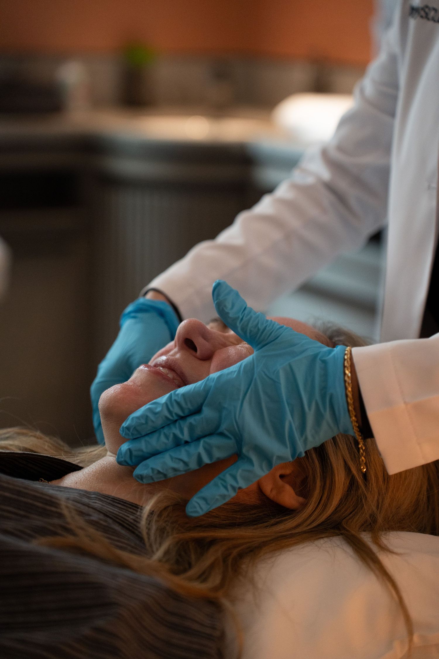Dermatologist in blue latex gloves performing a facial skin treatment on a female patient.