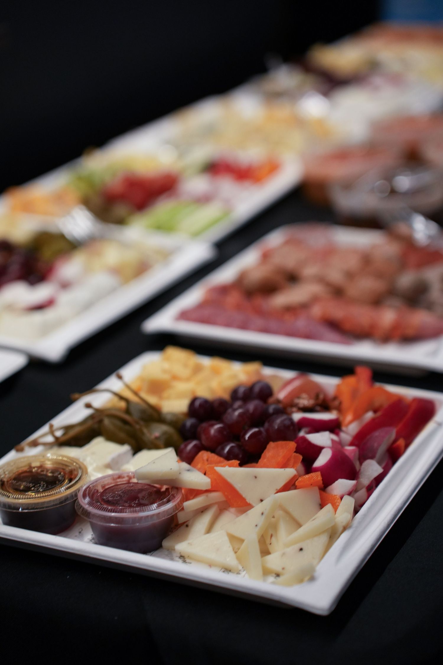 Elegant charcuterie and cheese board spread with grapes, vegetables, and dipping sauces at an event.