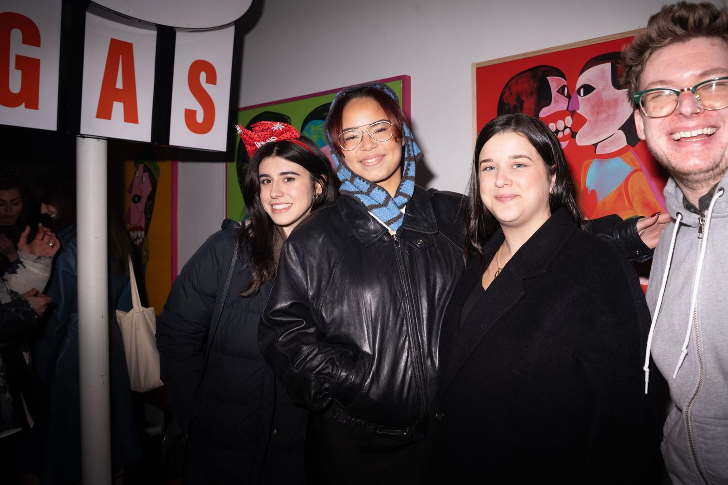 Four people smiling together at an art gallery with a GAS sign and colorful artwork in background.