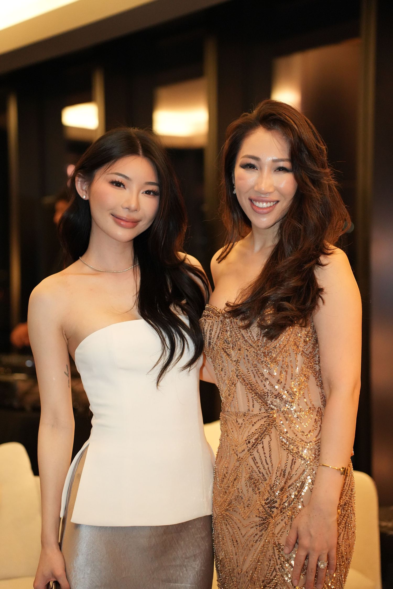 Two women in elegant formal attire smiling together at a glamorous evening celebration.