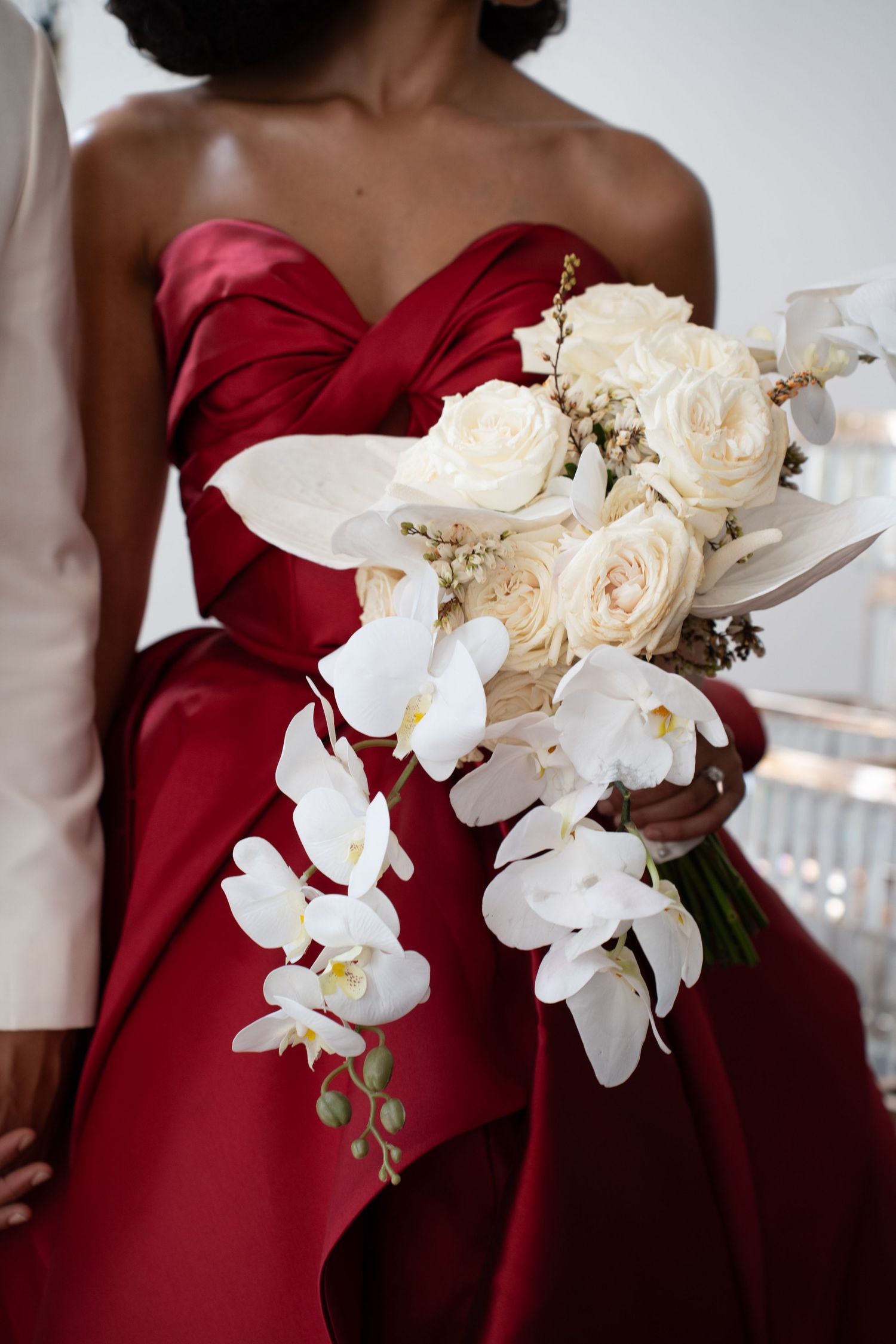 Bride in red strapless satin gown holding stunning cascading bouquet of white roses, calla lilies, and phalaenopsis orchids.