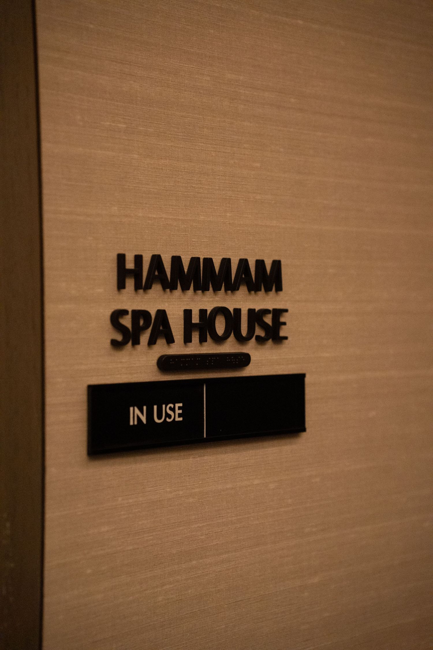 Hammam Spa House door sign with In Use indicator on a beige textured wall.