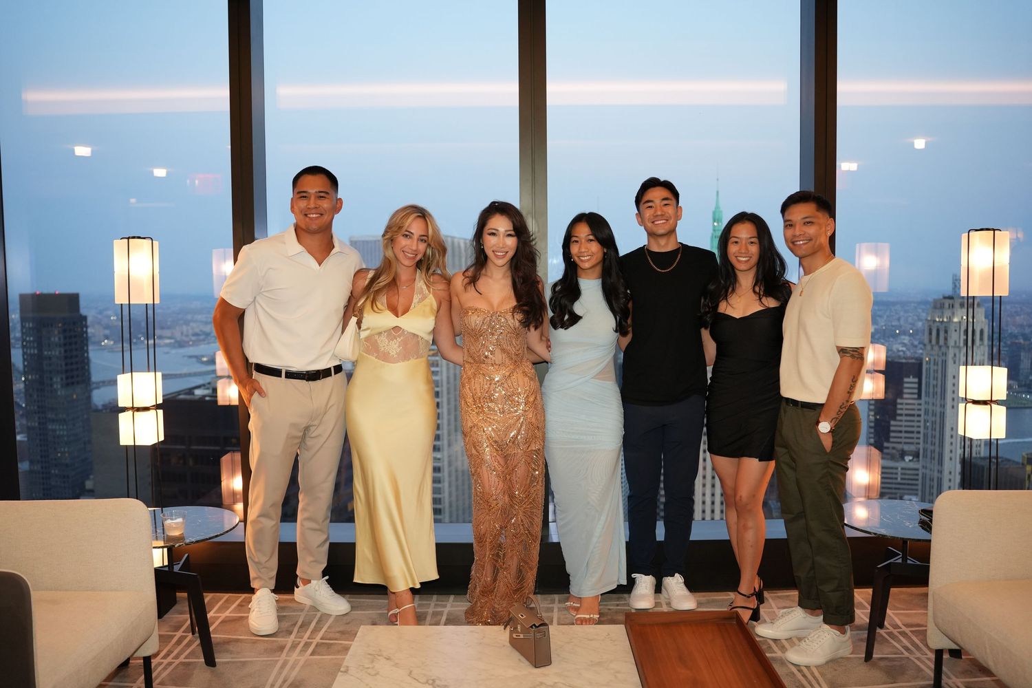 Group of seven friends posing together at a stylish high-rise party with city skyline backdrop.