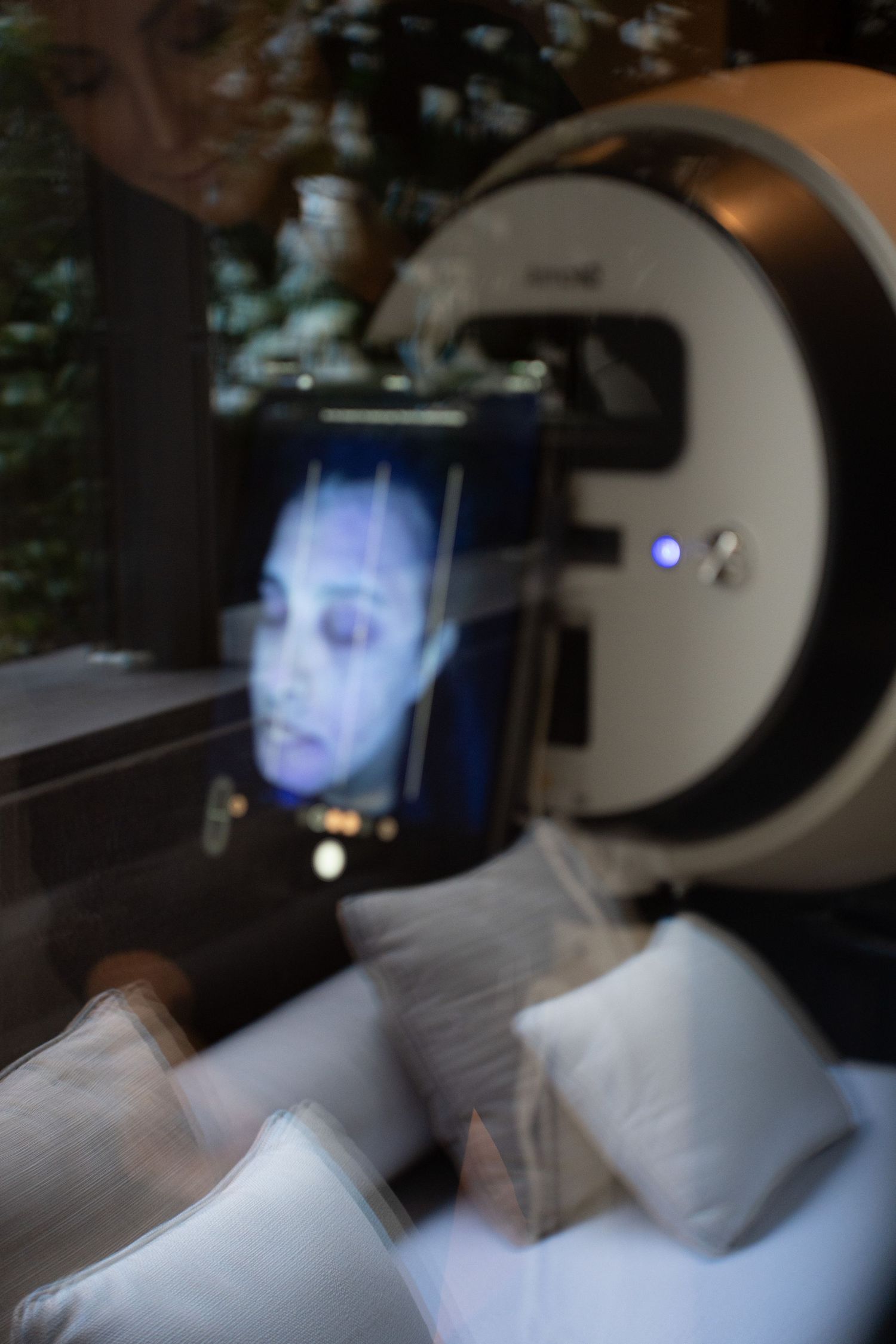 Person's face reflected on an Alma IQ skin analysis device screen in a dimly lit spa room.
