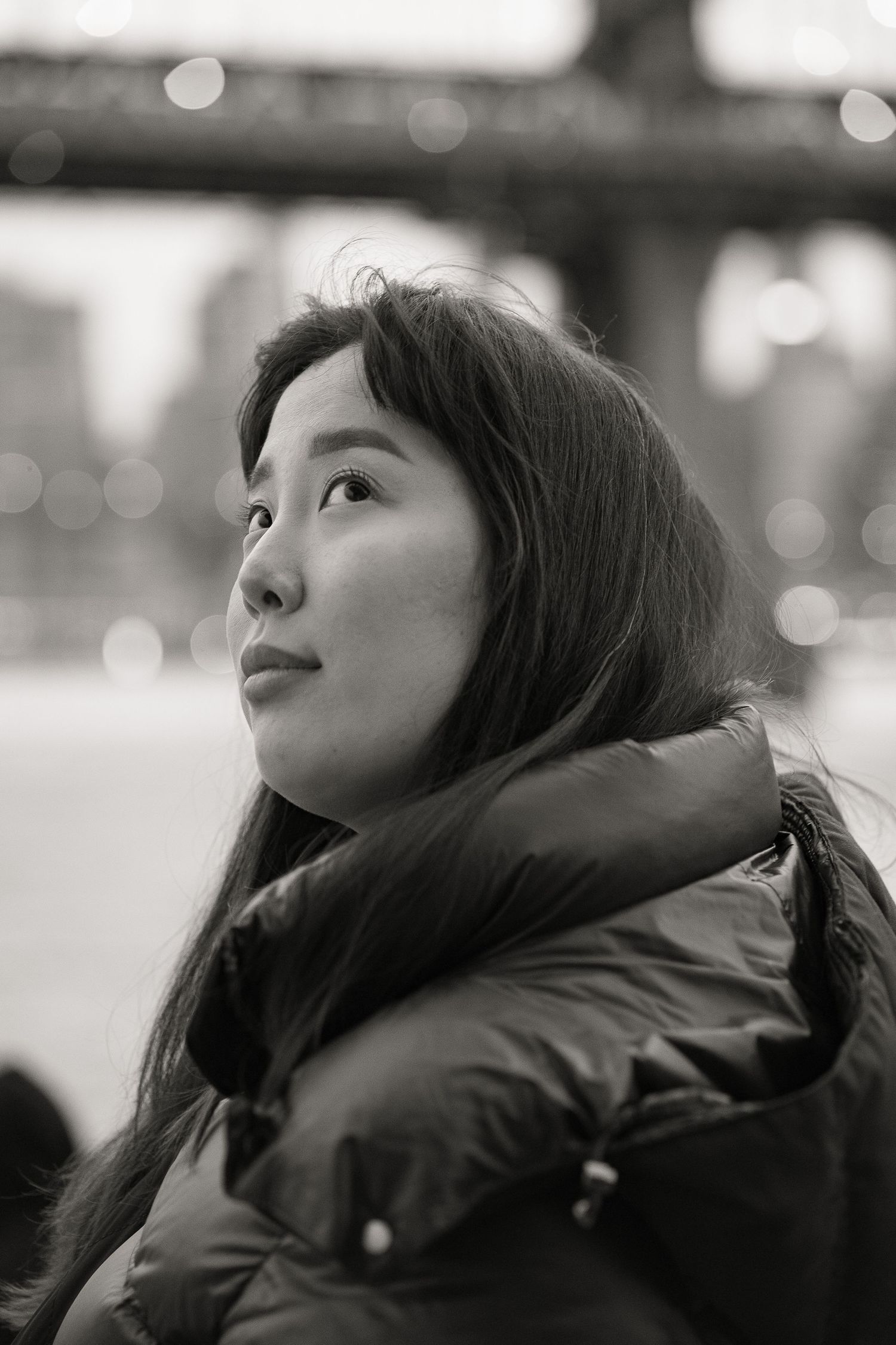 Young Asian woman gazing upward in black and white portrait near a bridge in New York City.