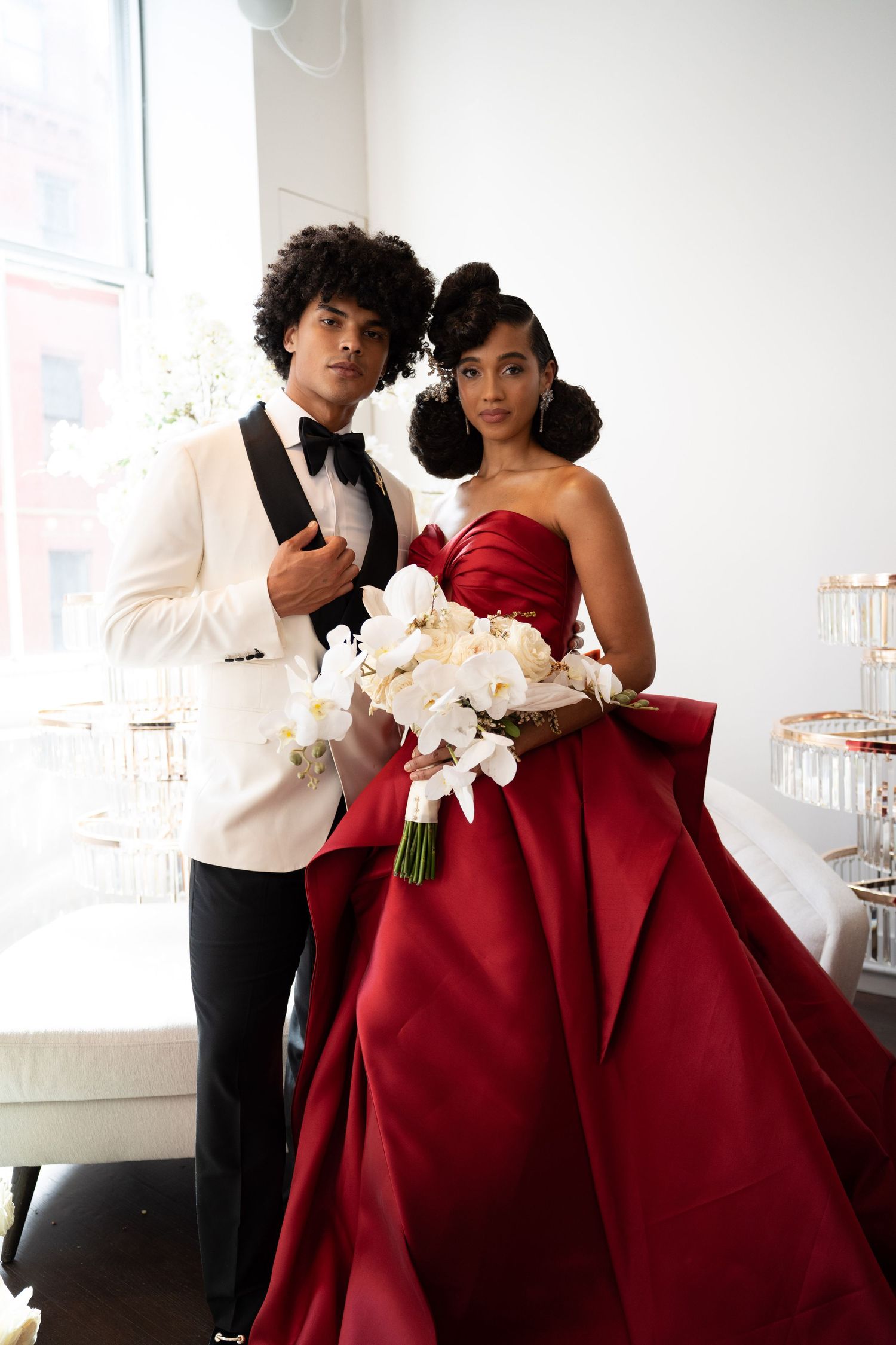 Elegant Black couple in wedding attire, bride holding white orchid bouquet in stunning red satin ball gown.