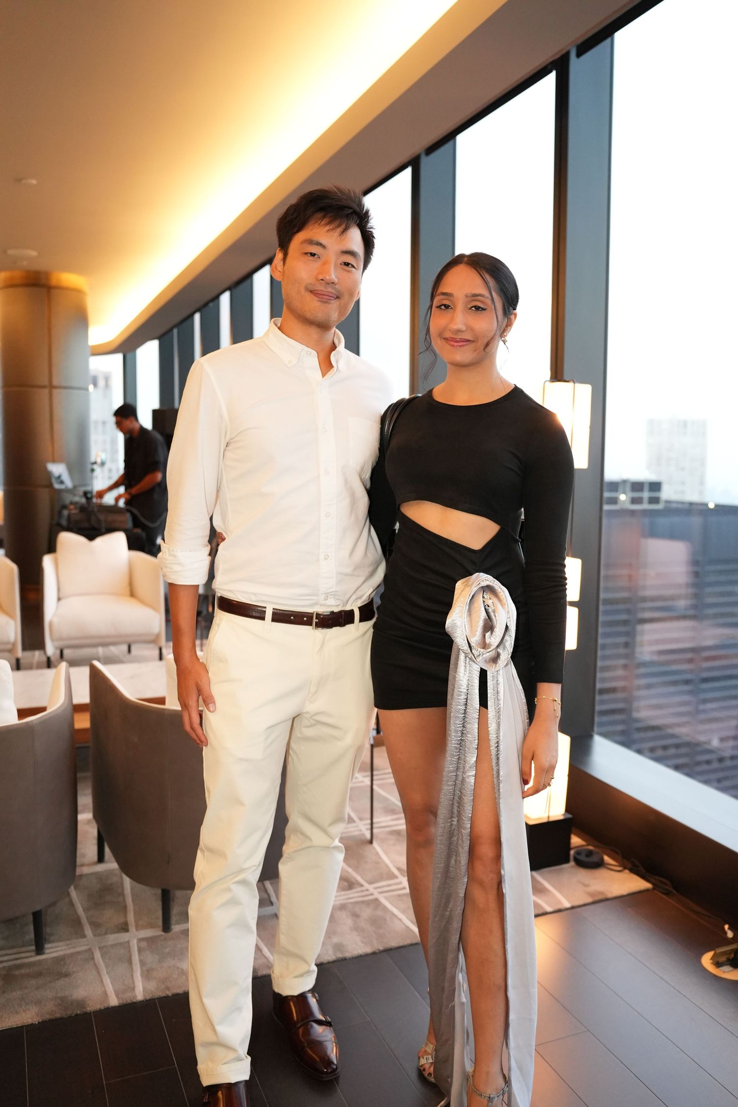Stylish couple posing in a modern upscale venue with large windows overlooking the city.