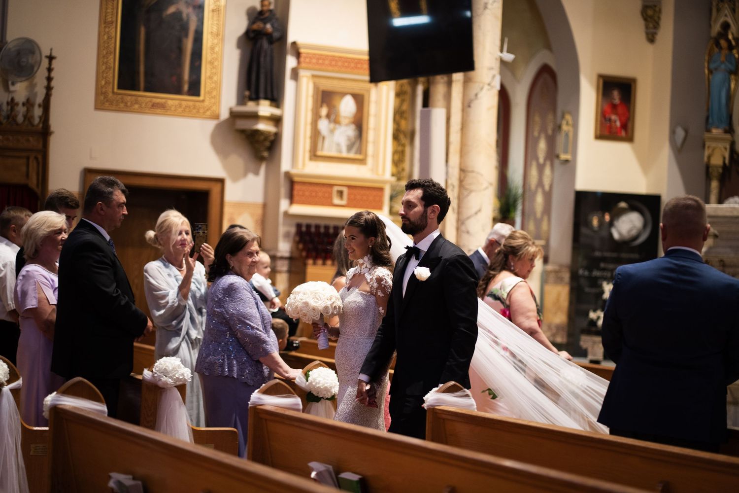 Wedding party gathers in ornate church as bride and groom prepare to walk the aisle.