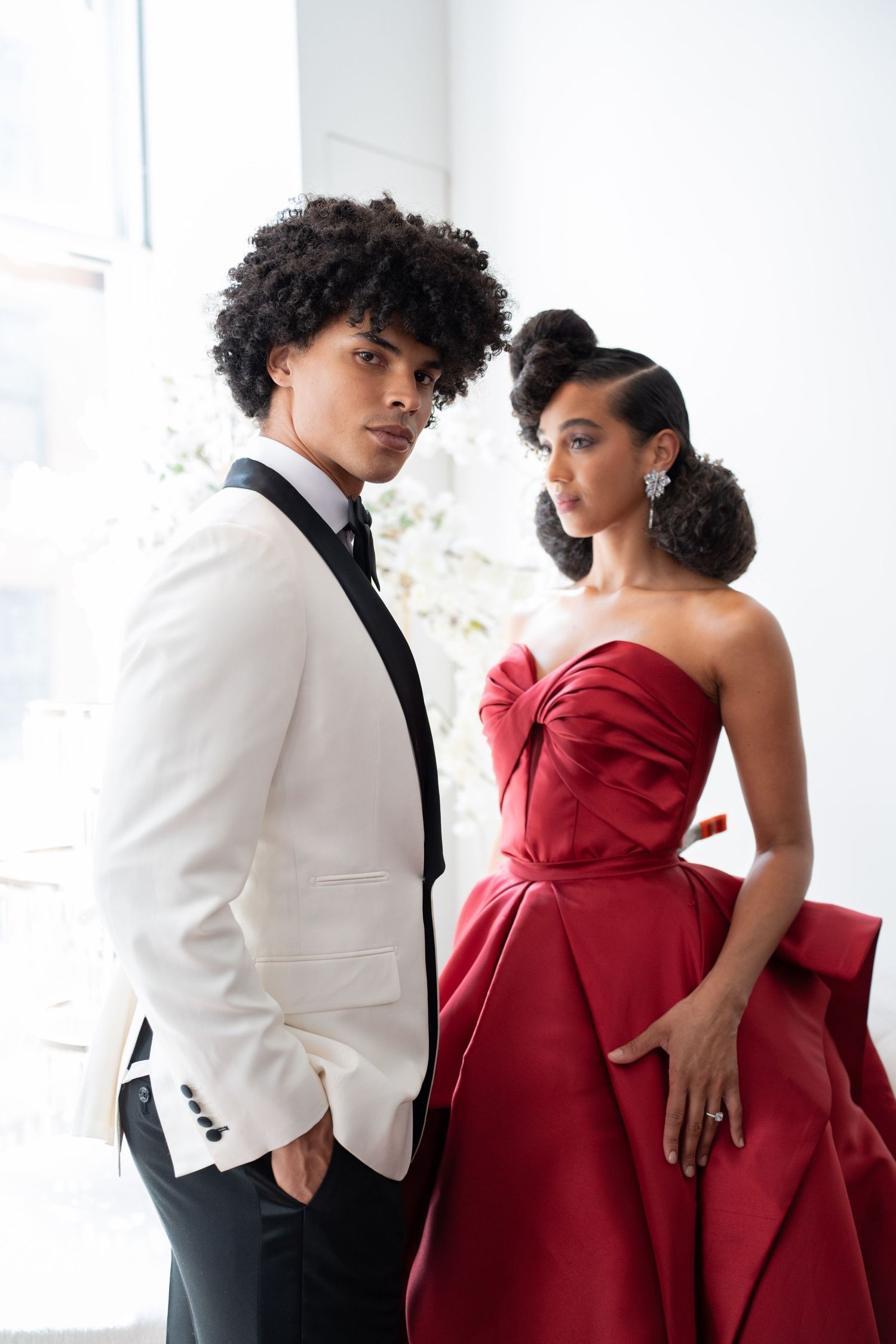 Sophisticated couple posing in white tuxedo and red ballgown at bright wedding venue.