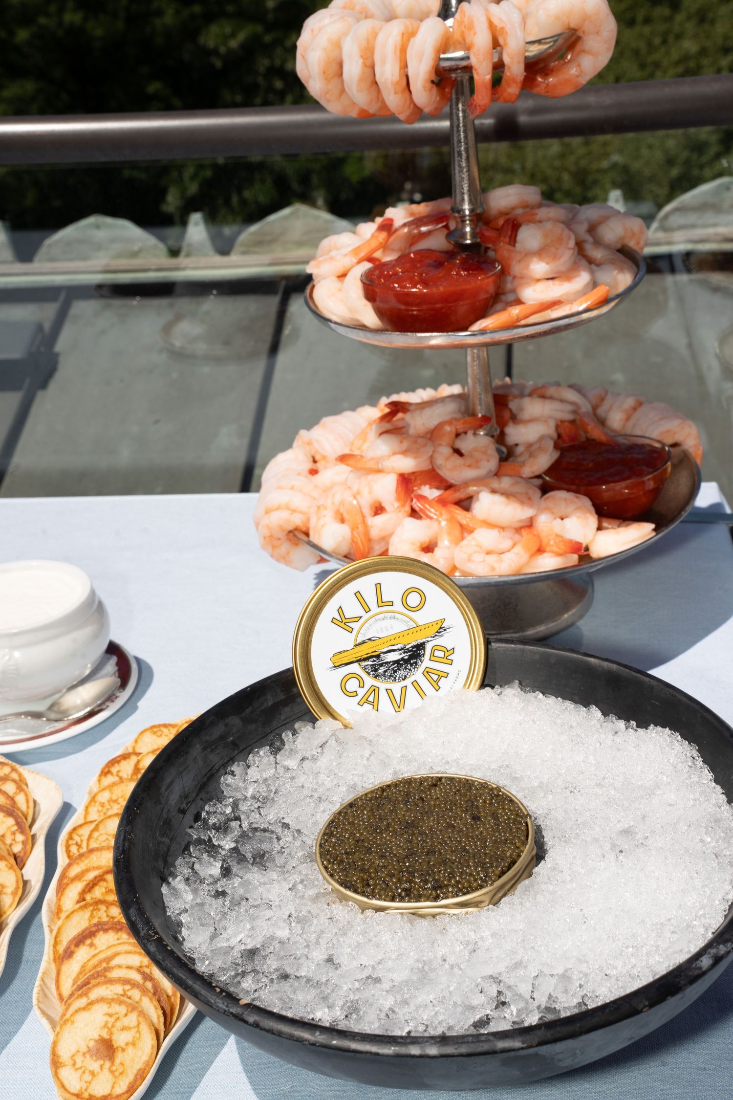 Kilo Caviar tin displayed on ice beside shrimp cocktail tower at luxury outdoor rooftop dining event.