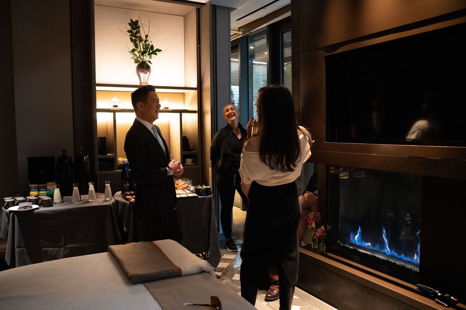 People networking in a modern luxury spa showroom with a fireplace and product displays.