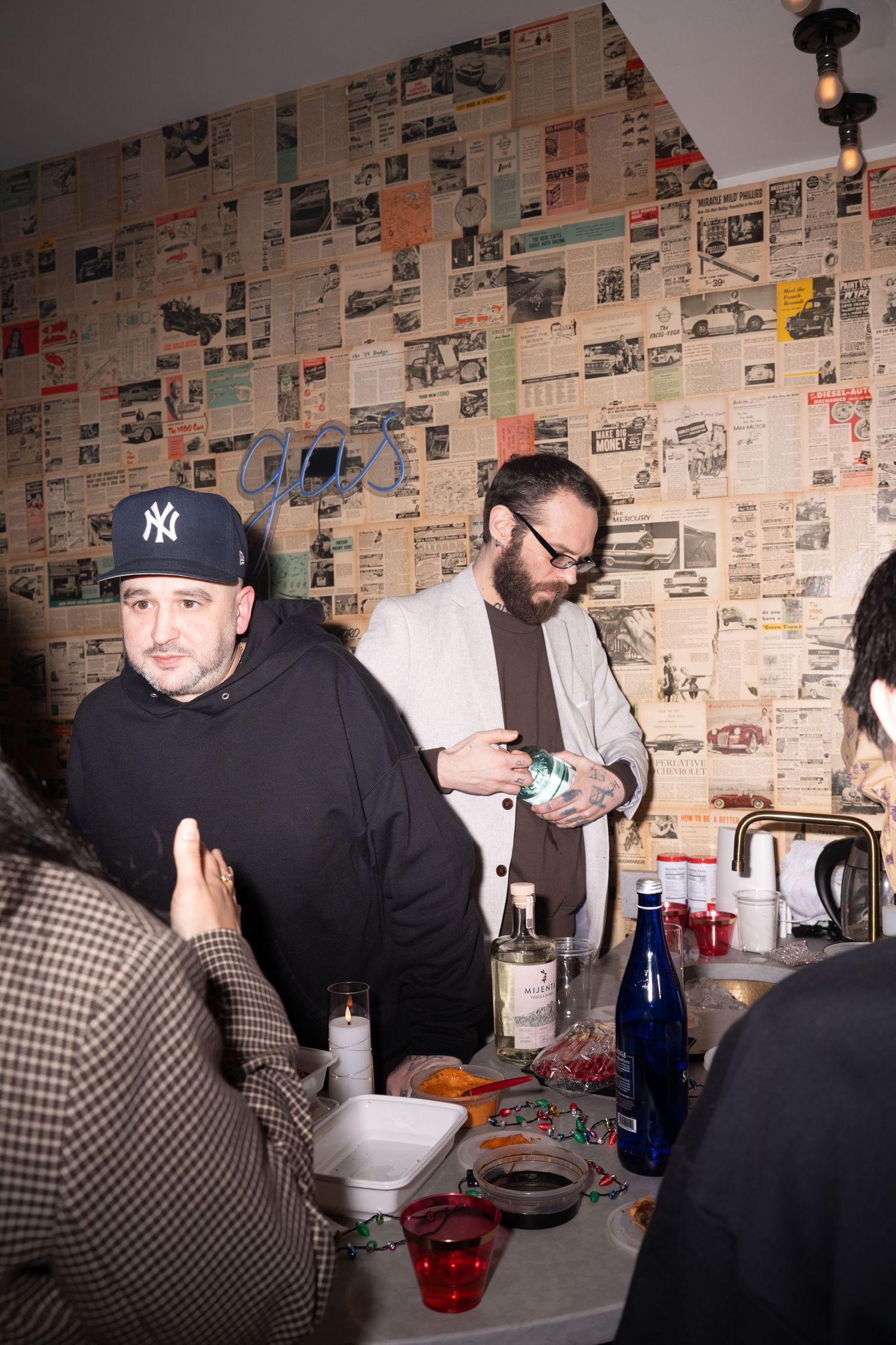 People gathered around a bar area with newspaper-covered walls at a casual holiday party.