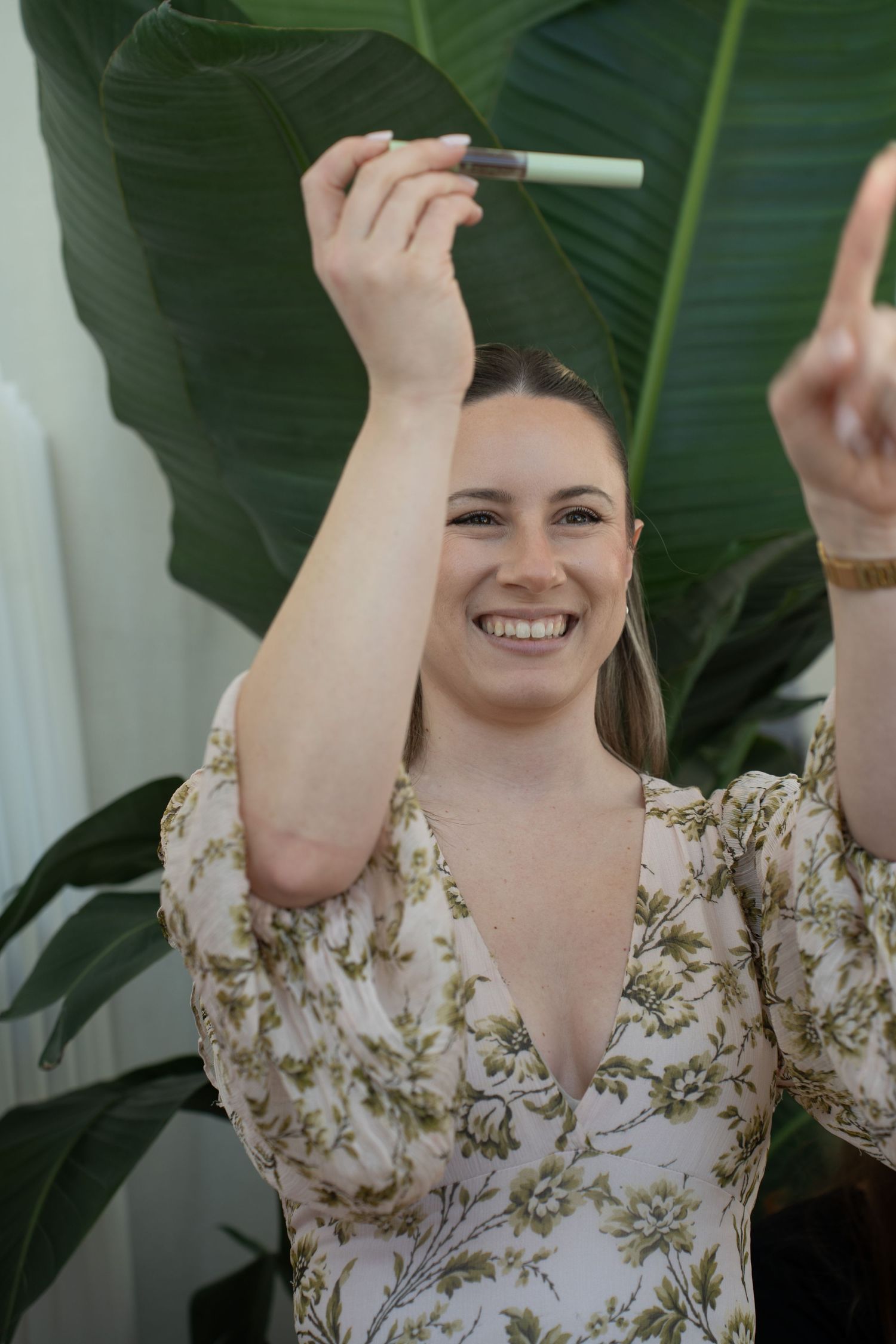 Smiling woman in floral dress holding up a makeup product at a Pixi beauty promotional event.
