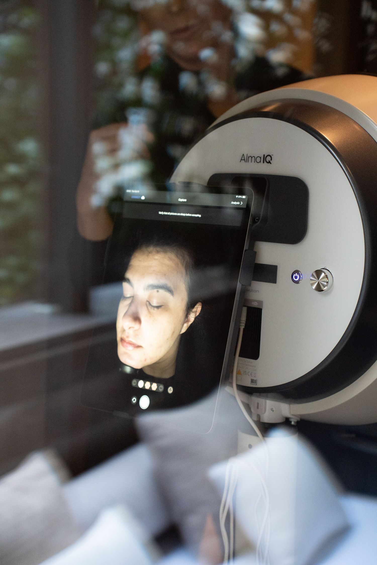 Close-up of Alma IQ facial skin analysis device displaying a patient's face scan results.