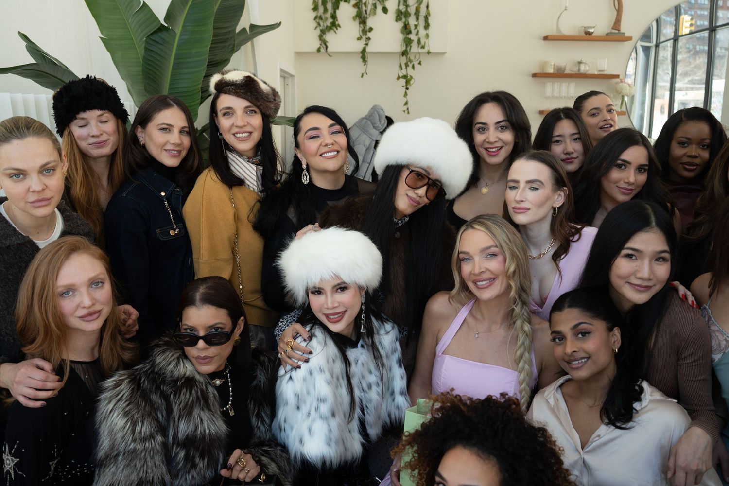 A large group of diverse women smile together at an indoor beauty event gathering.