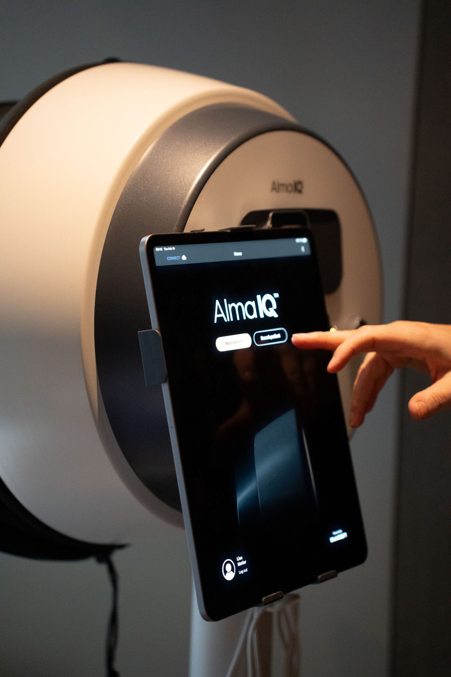 Hand touching the Alma IQ touchscreen interface on a white medical aesthetic device.