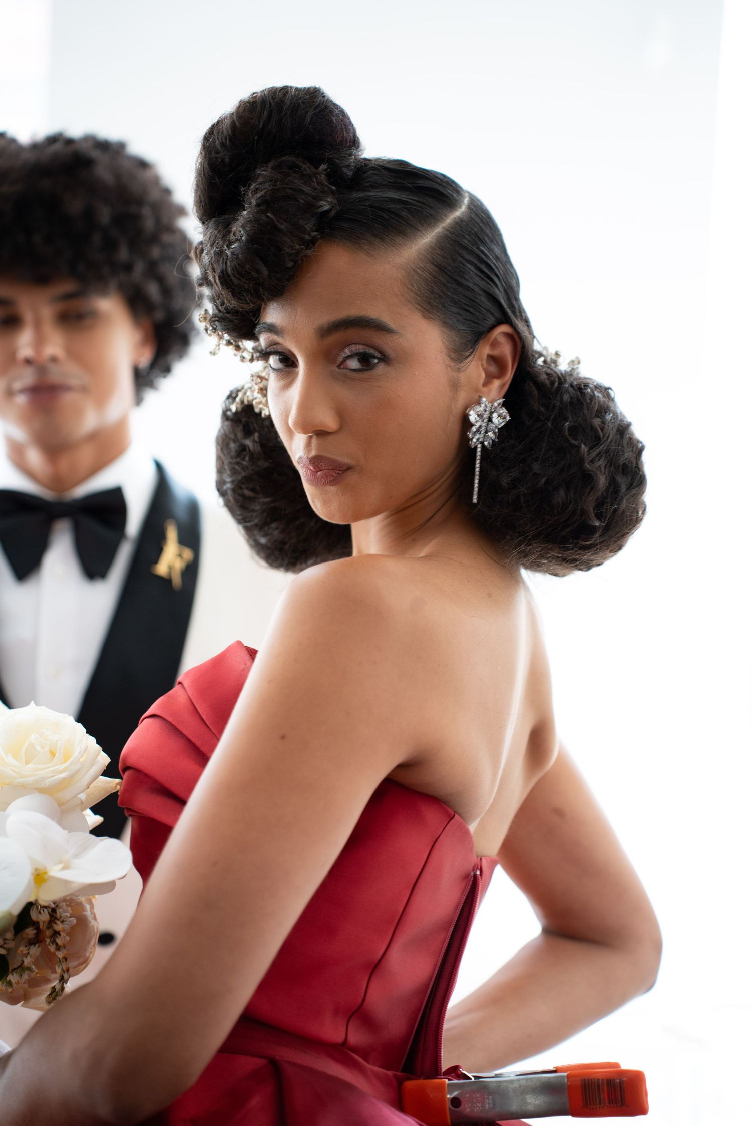 Beautiful bride in red strapless gown with dramatic curled updo and sparkling drop earrings posing at wedding.