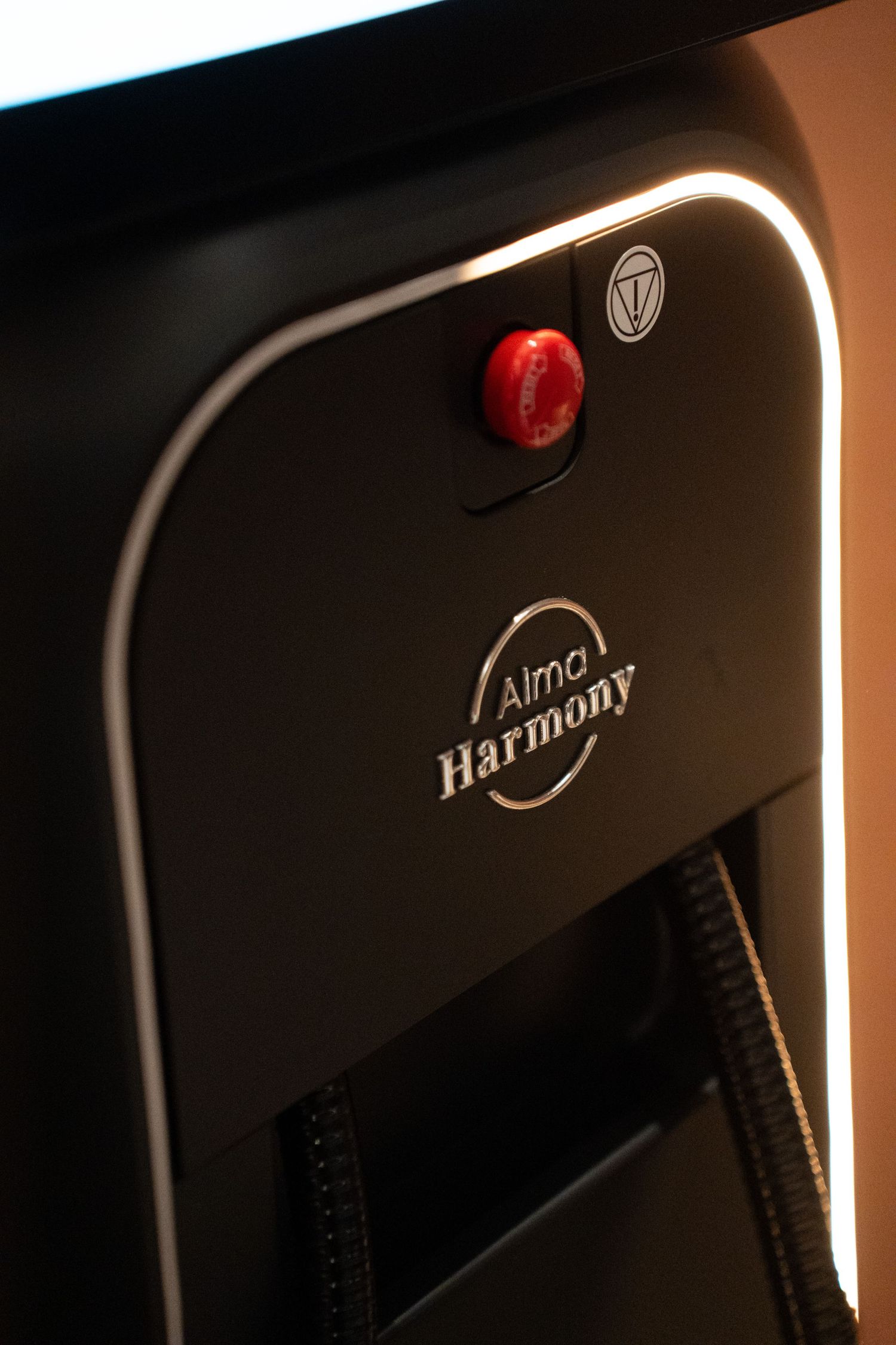 Close-up of Alma Harmony laser device with red button and branded logo in dark treatment room.