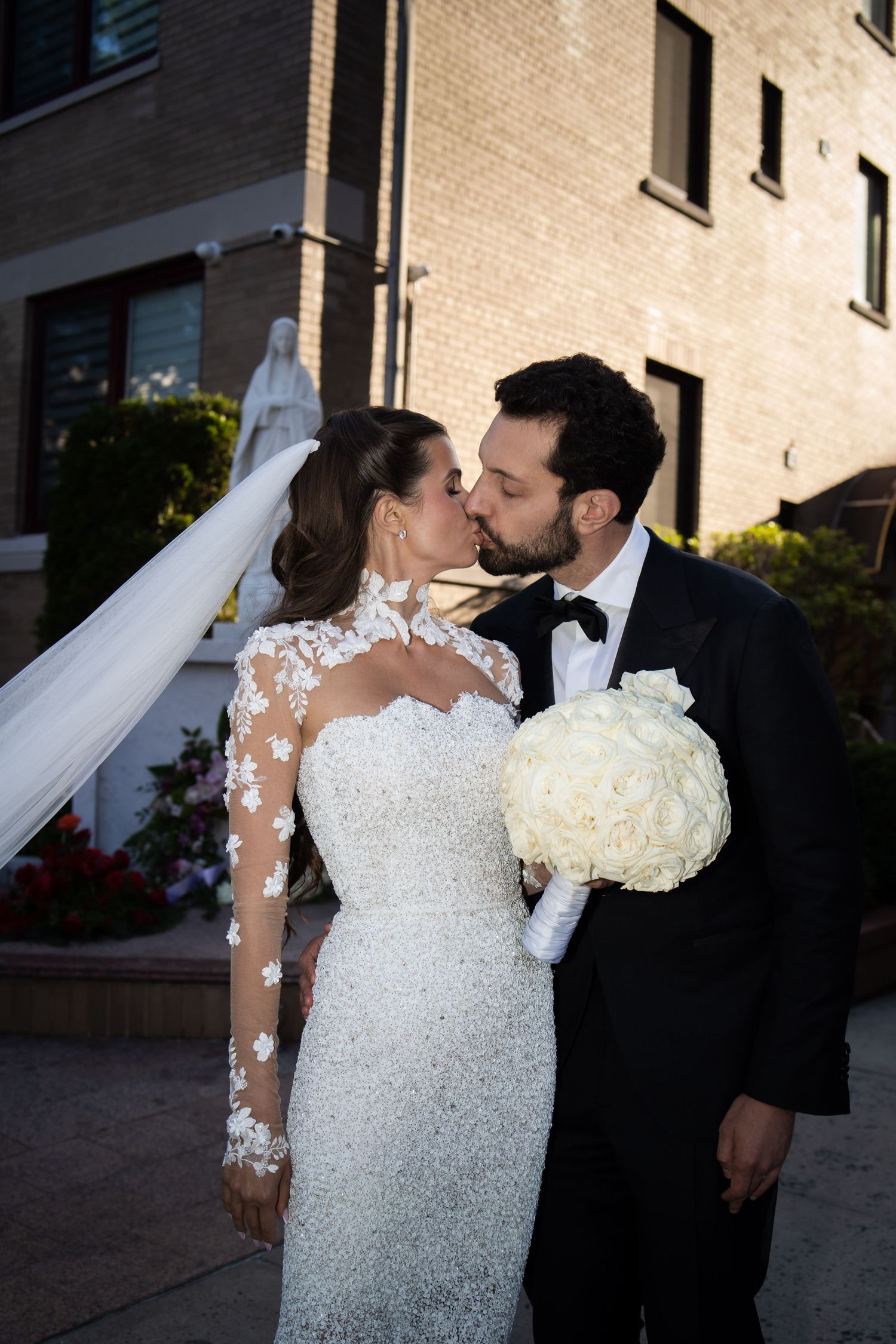 Couple kisses after wedding ceremony, bride in long-sleeve beaded gown with floral lace details.