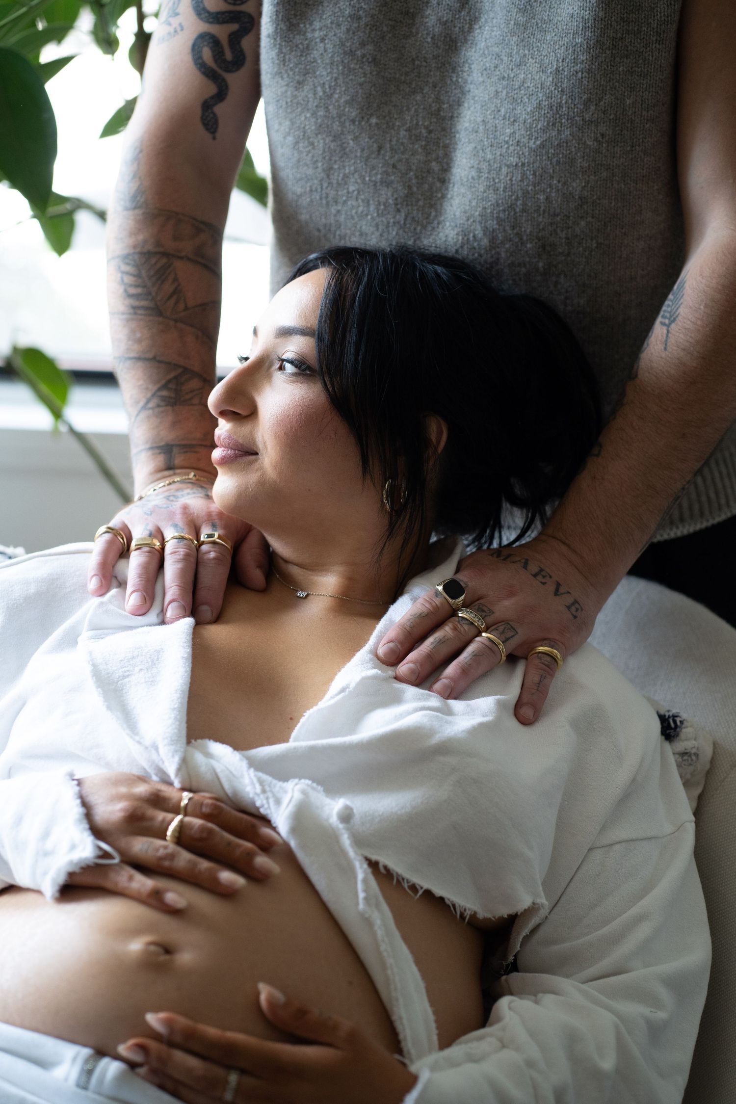 Tattooed man placing hands on smiling pregnant woman's shoulders as she cradles her belly.