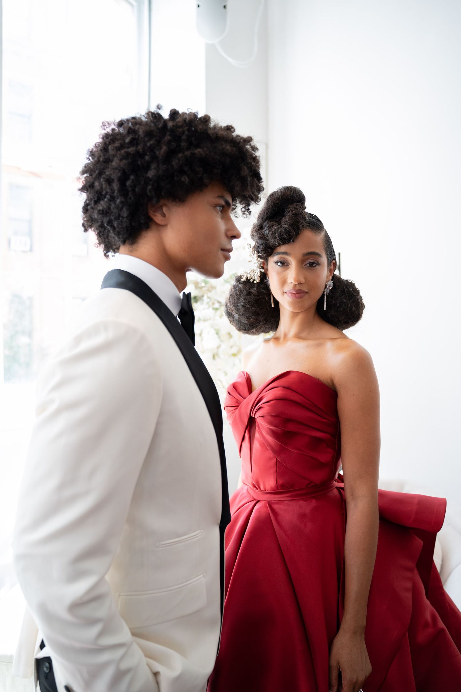 Stylish Black couple posing in formal wear, man in white tuxedo and woman in red strapless gown.