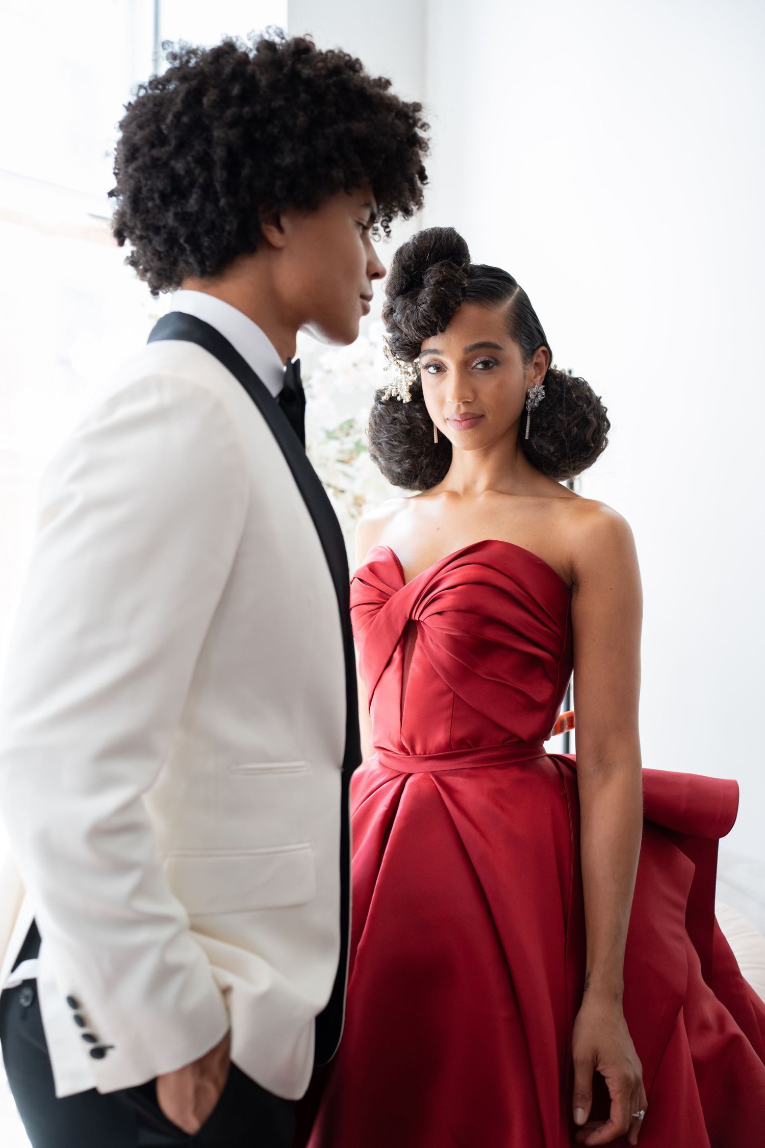 Fashionable wedding couple with bride in red strapless gown and groom in white tuxedo.