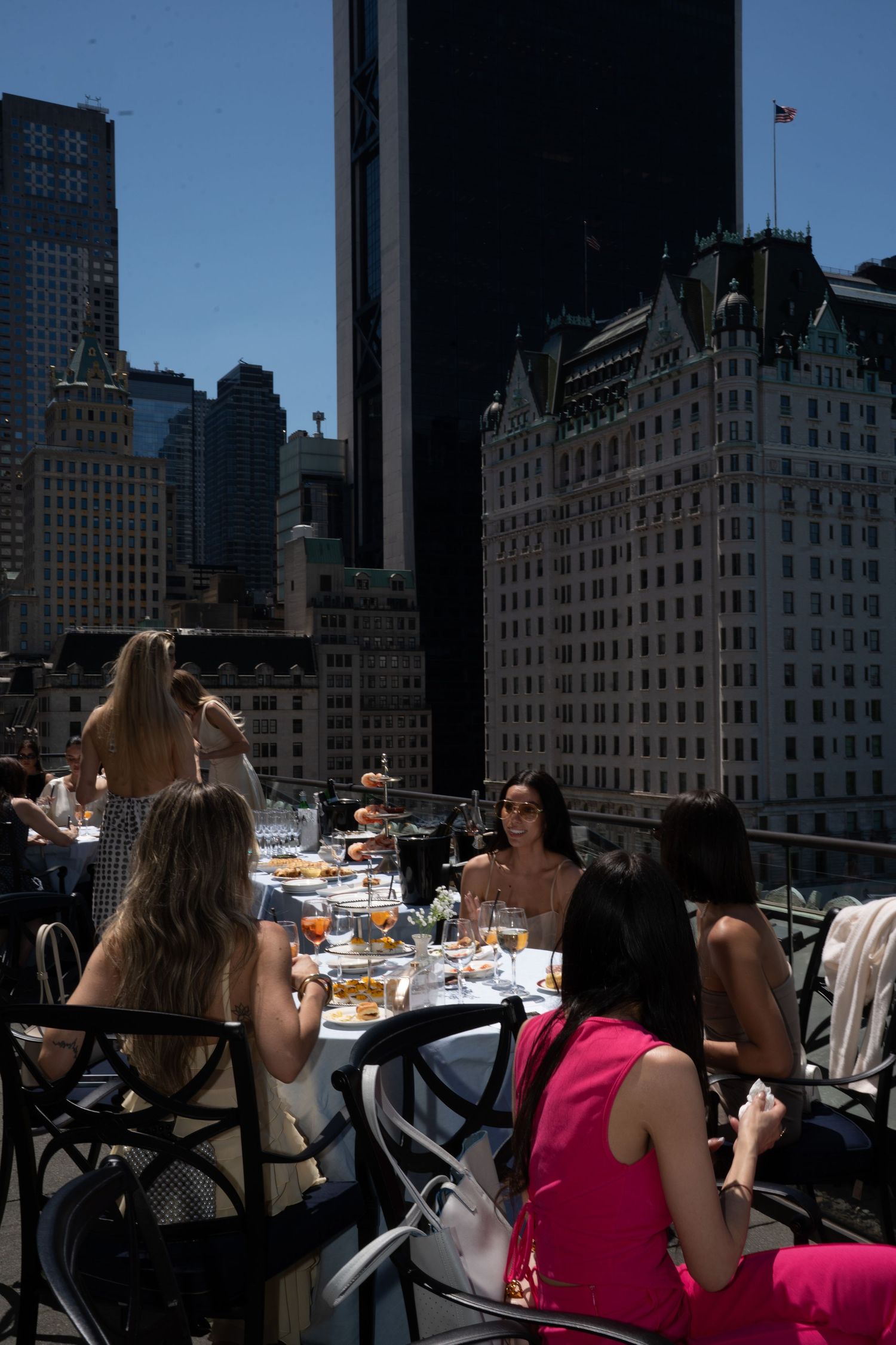 Women dining at outdoor rooftop restaurant with stunning New York City skyscraper views.