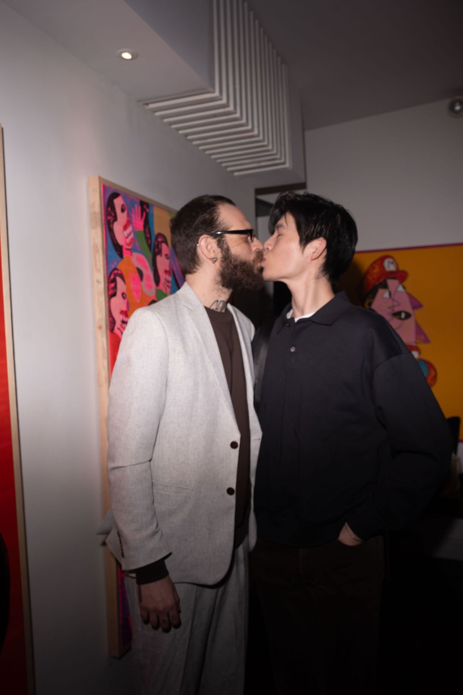 Couple shares a kiss in front of colorful pop art paintings at gallery.