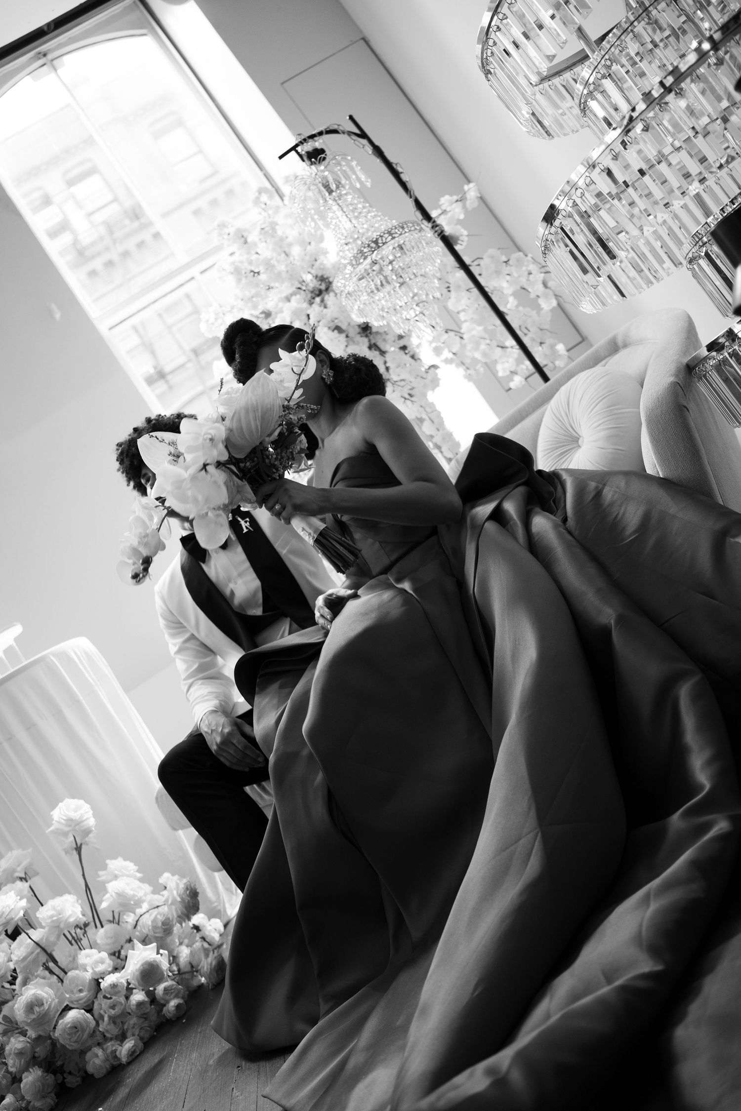 Black and white photo of a bride and groom sharing a kiss at their elegant wedding reception with floral arrangements.