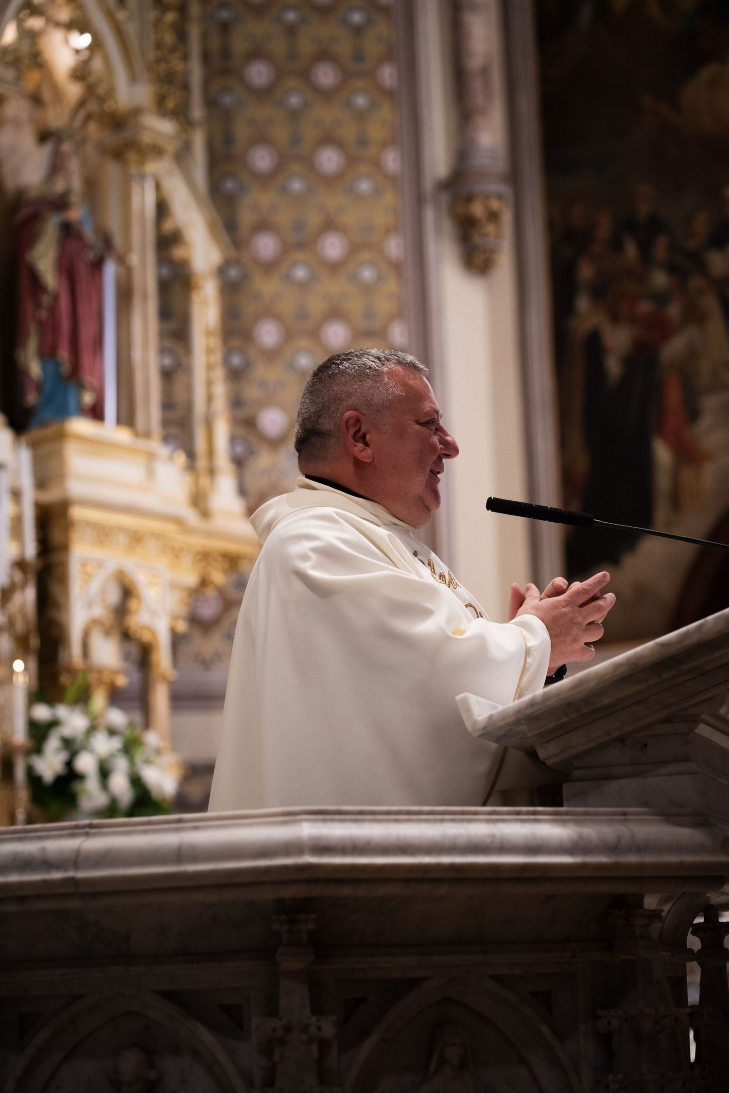 Catholic priest delivers homily at ornate golden altar podium during elegant church wedding ceremony.