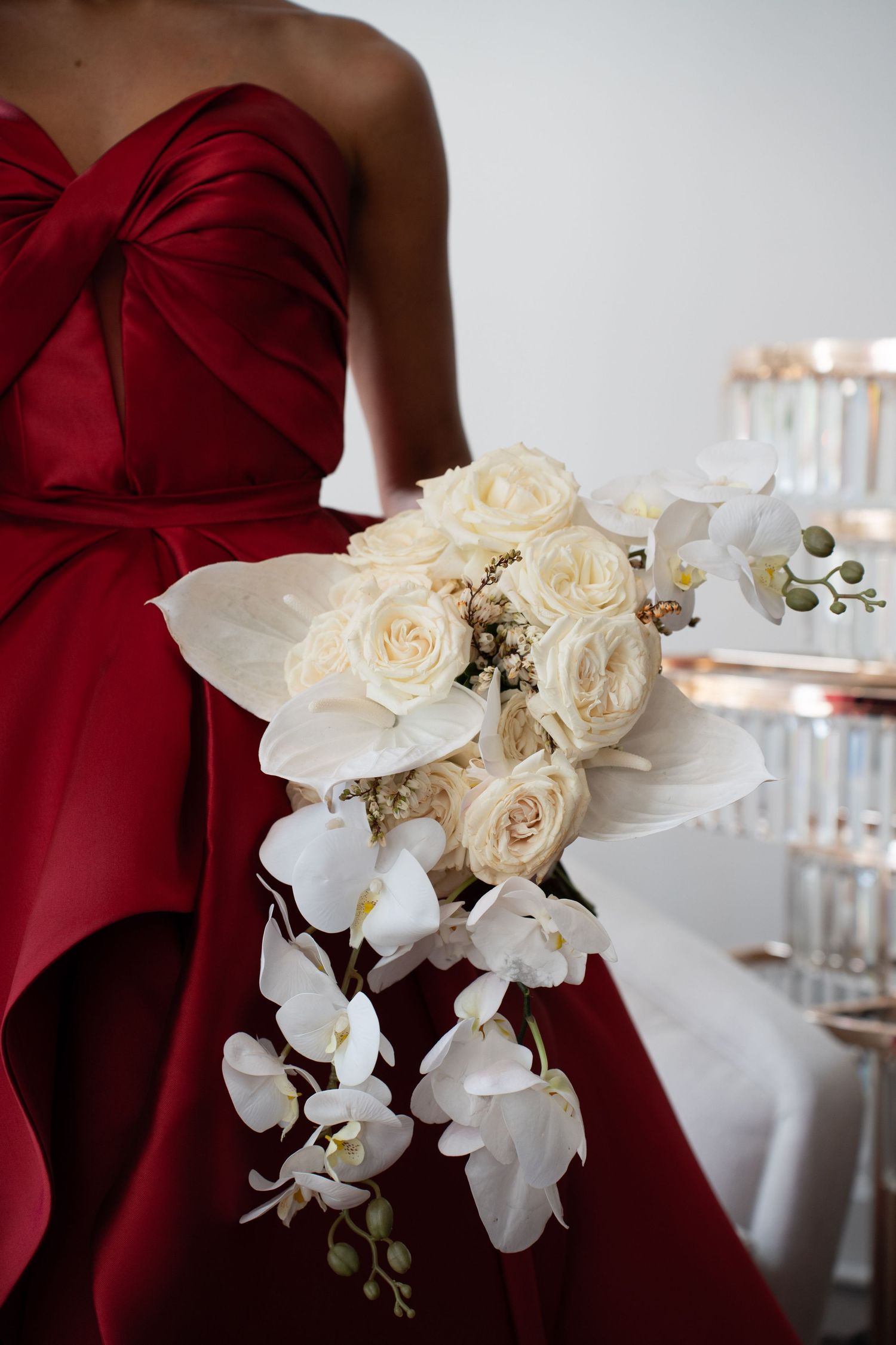 Close-up of bride in red strapless satin gown holding cascading bridal bouquet of white roses and phalaenopsis orchids.