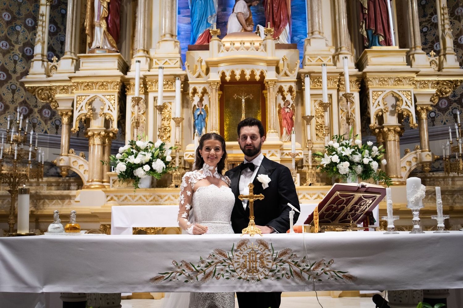 Bride and groom pose together at elaborately decorated gold church altar after ceremony.