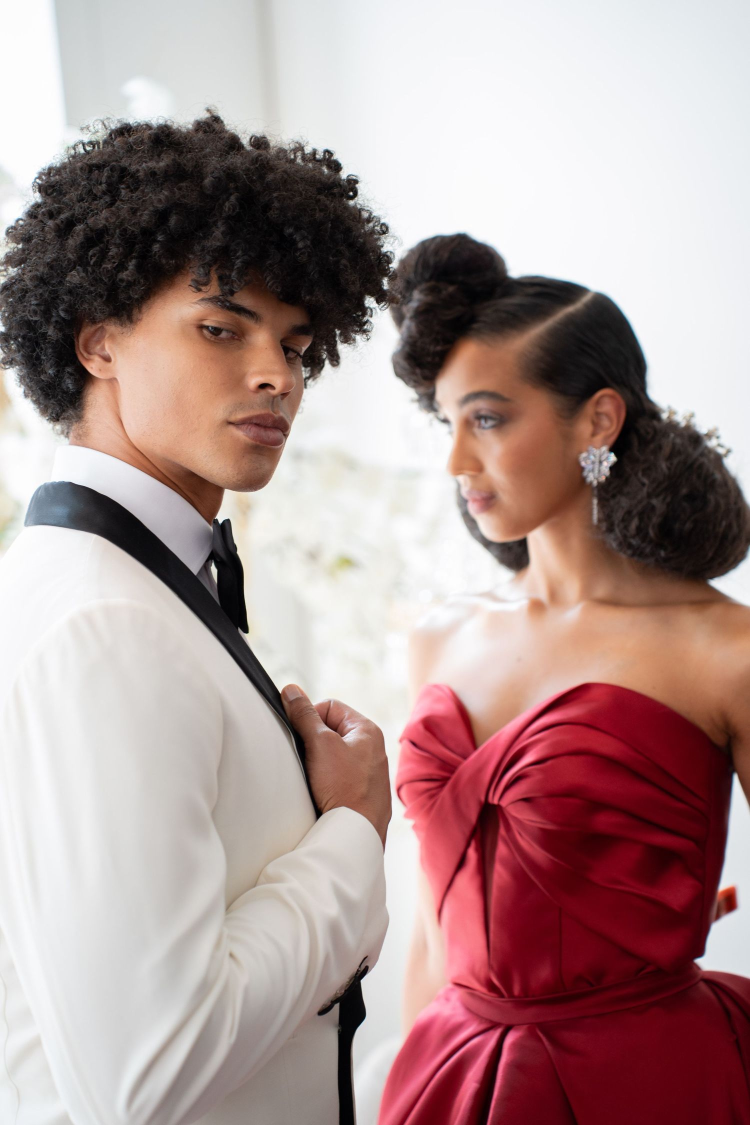 Close-up of couple in white tuxedo and red strapless gown at elegant wedding shoot.