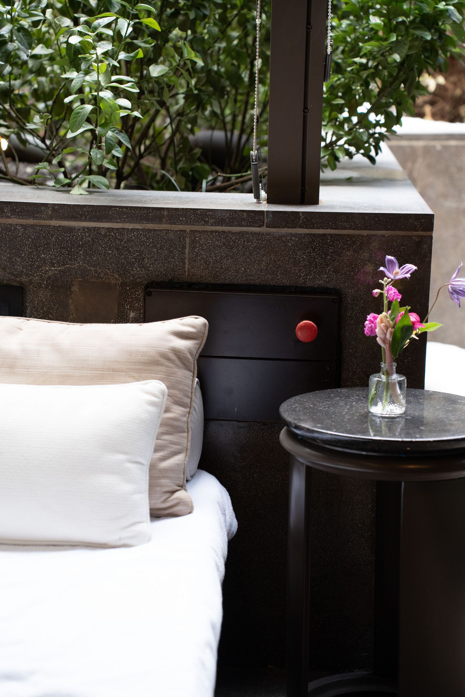 Elegant outdoor lounge seating with white cushions and purple flowers on dark marble side table.