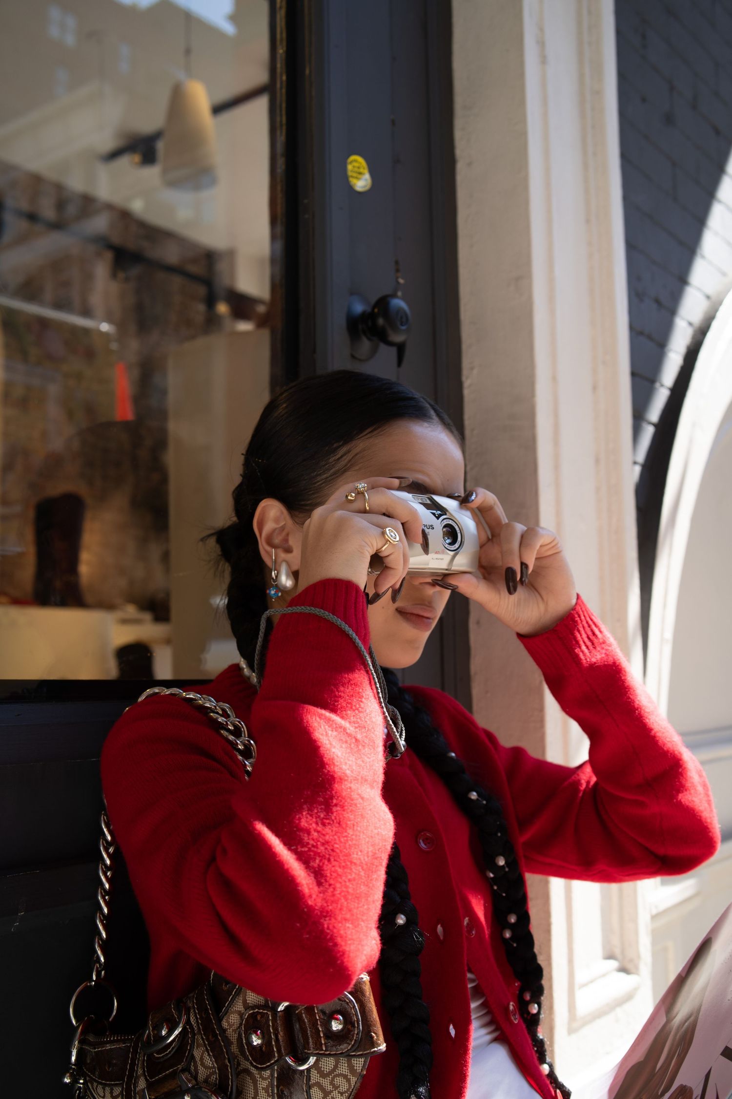 Woman in red cardigan photographing with vintage camera outside urban storefront.