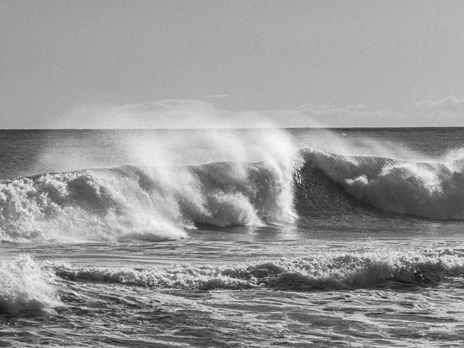 High contrast monochrome image of massive waves breaking with sea spray in stormy conditions.