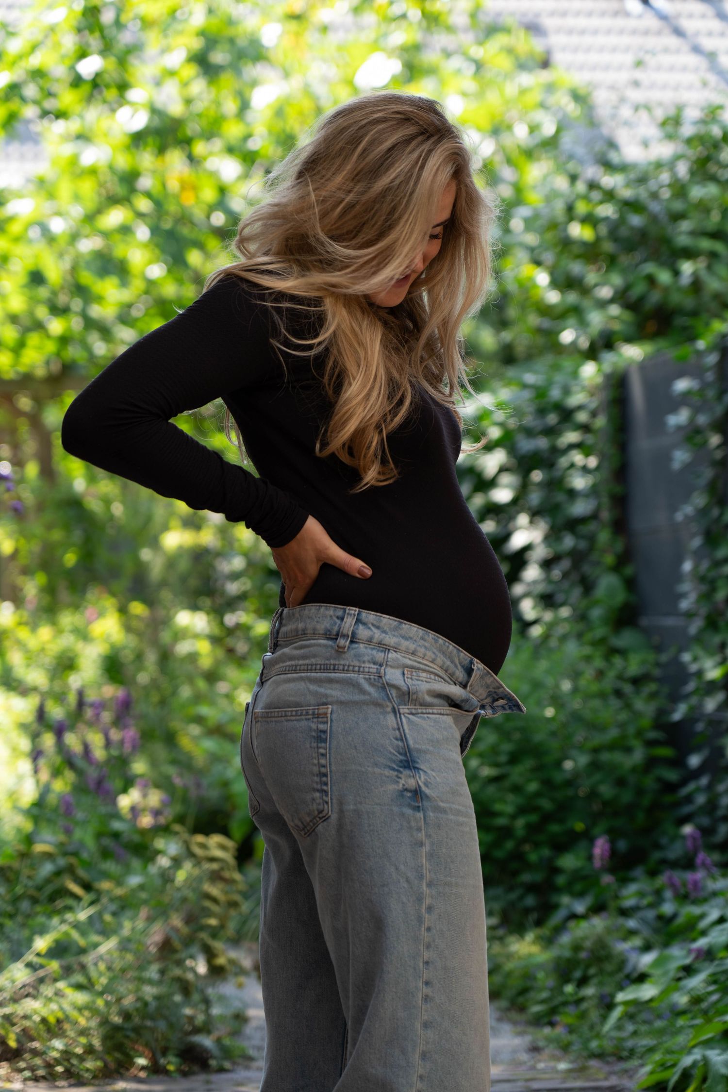 Zwangere vrouw in zwarte trui en jeans in haar tuin.
