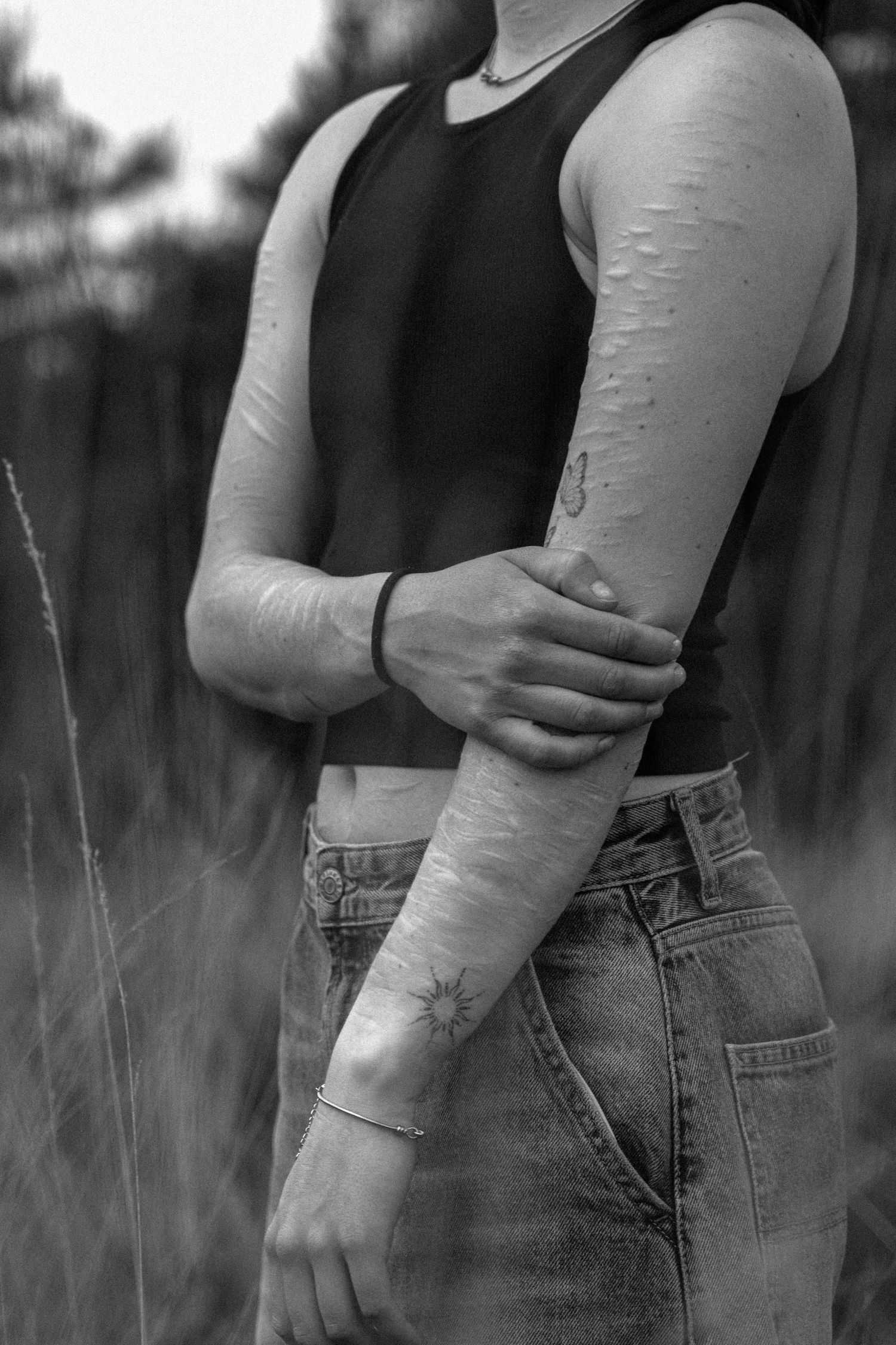 Black and white close-up of arm with delicate tattoos and black tank top.