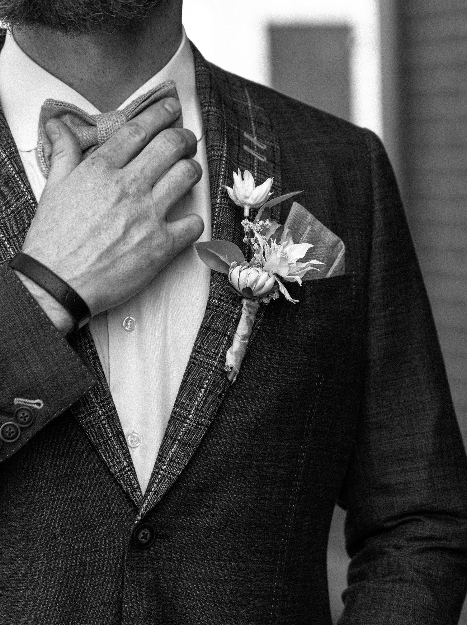 Detail trouwcorsage met witte bloem op donker pak.