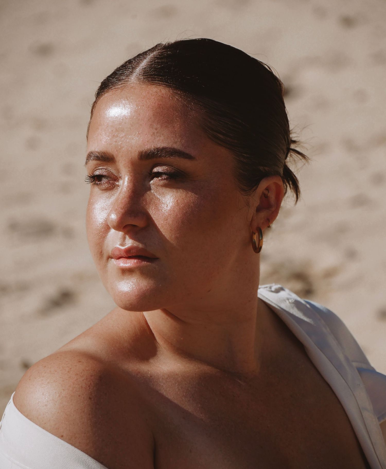 Zonovergoten portret op het strand in witte off-shoulder top.