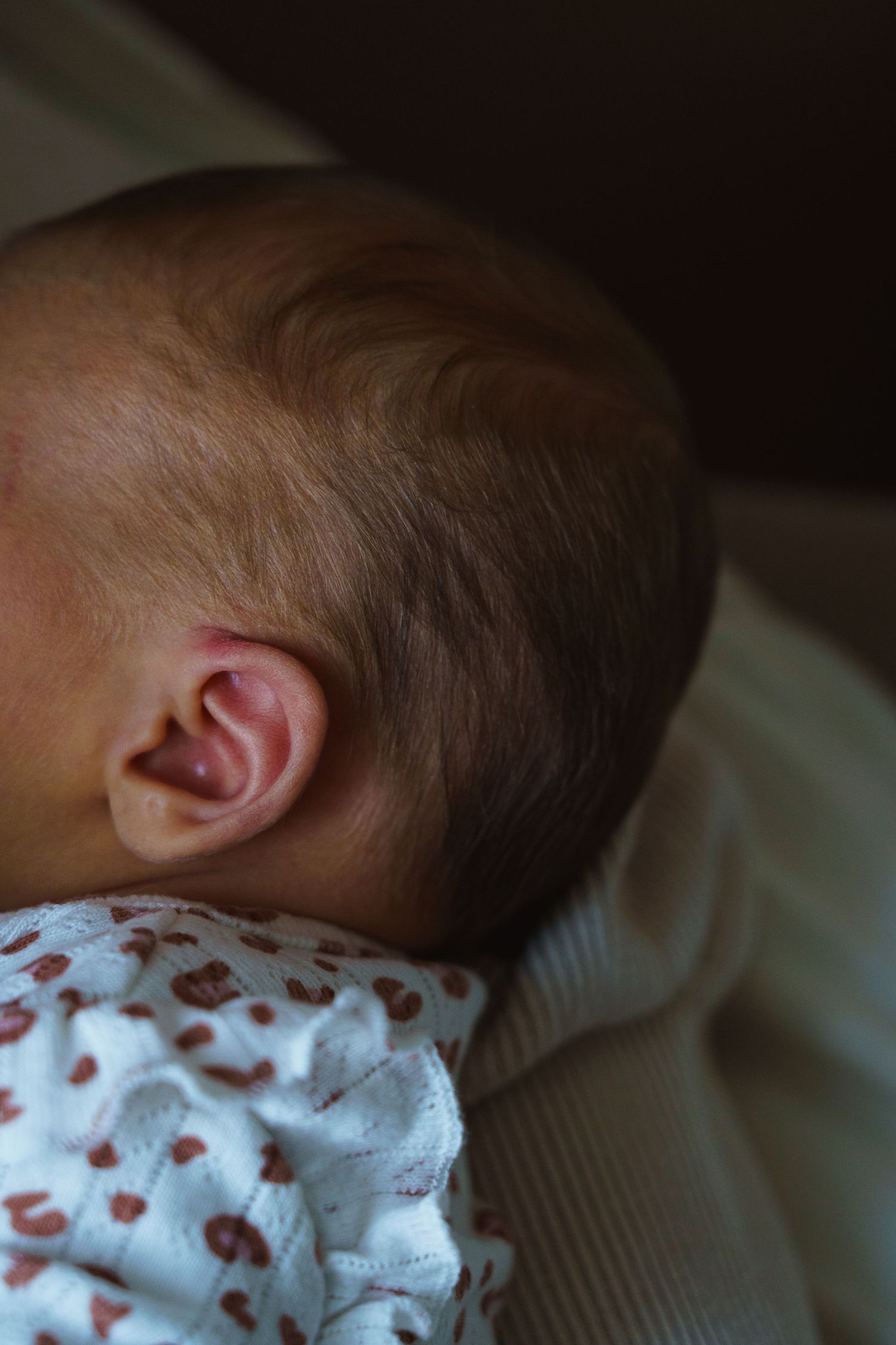 Sleeping baby wearing white clothing with red hearts pattern rests peacefully in soft lighting.