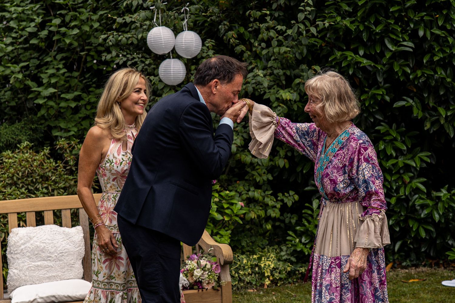 A group of wedding guests dance and celebrate together outdoors at a garden reception.