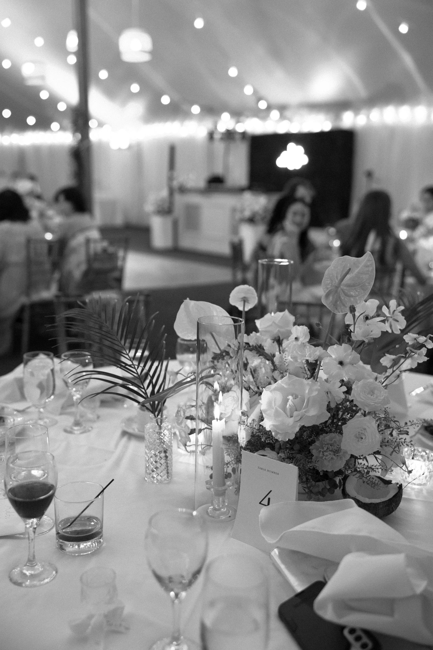 Elegant wedding reception tables decorated with white floral centerpieces, glowing candles and crystal glassware in a tent.