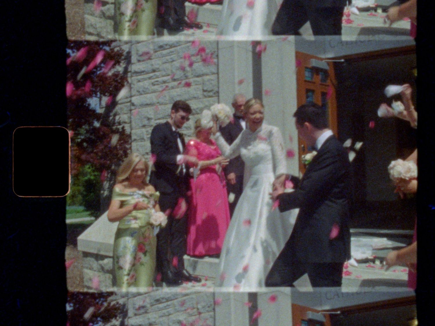 A joyful outdoor wedding ceremony with guests throwing pink rose petals on the bride in a white gown.