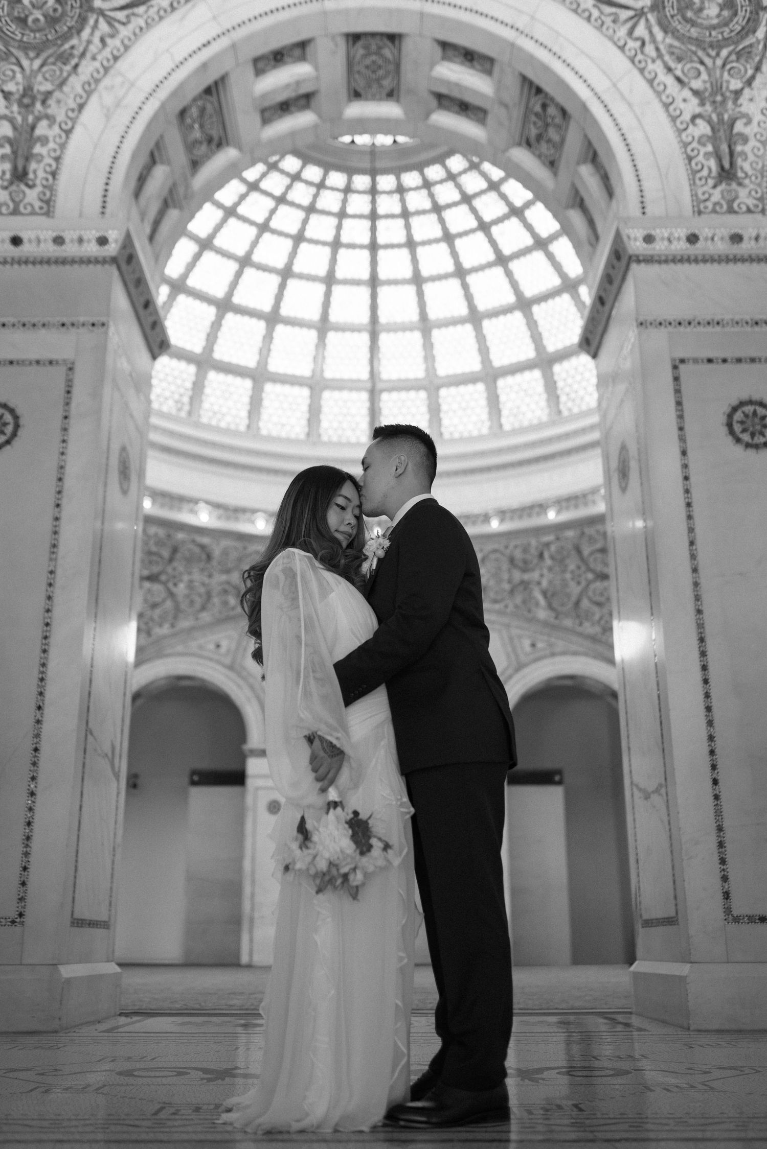 A couple shares intimate moments during their wedding photoshoot in an ornate domed room with classical architecture.