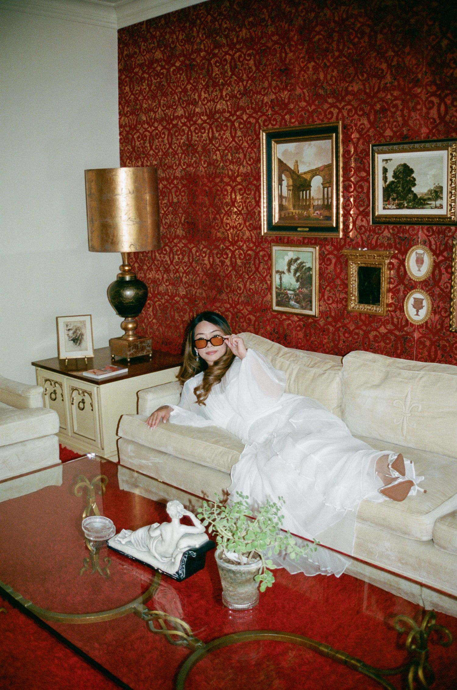 A sequence of photos showing a person in a white dress reclining on a red couch with vintage decor and artwork on the walls.