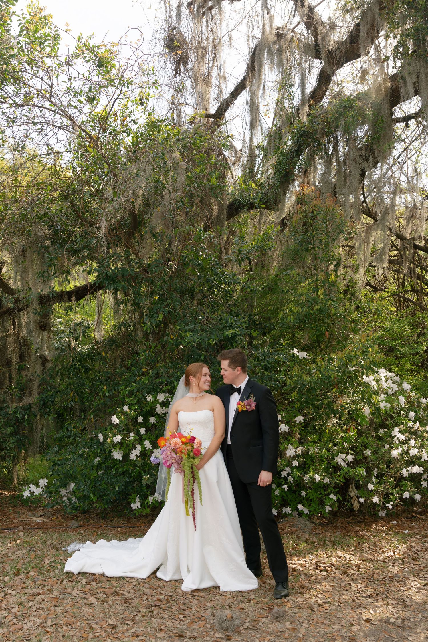 Bride and groom share a romantic moment under Spanish moss-draped oak trees surrounded by blooming white azaleas.