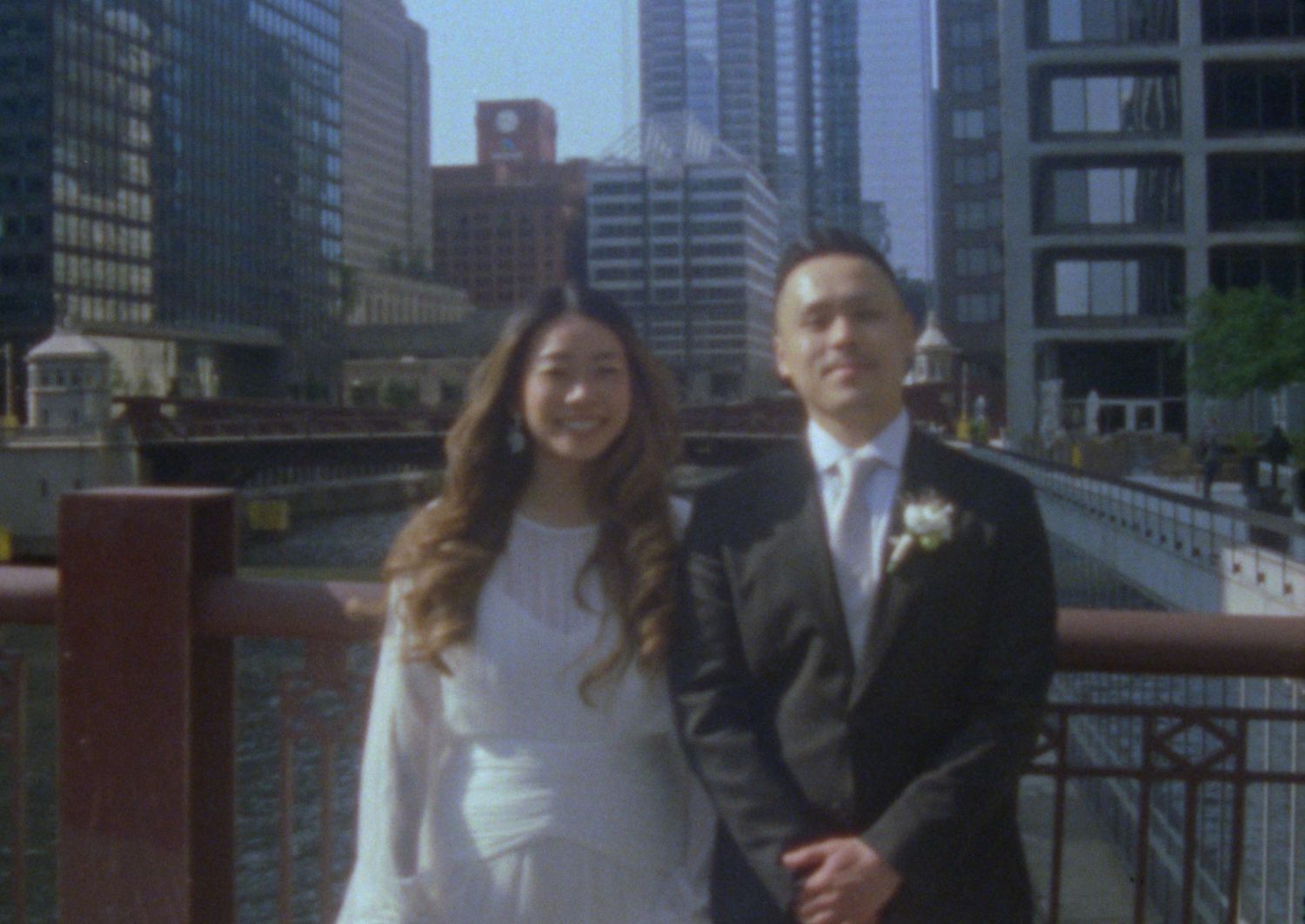A wedding party poses on a wooden deck overlooking a modern city skyline with skyscrapers in the background.